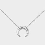 A moon necklace in sterling silver. The necklace features a delicate silver chain with a pendant in the shape of a crescent moon. The necklace is perfect for those who love celestial-inspired jewelry, and makes for an elegant and stylish accessory that can be worn on any occasion.