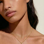 Close-up of a woman wearing a gold necklace with a moonstone pendant against a neutral background