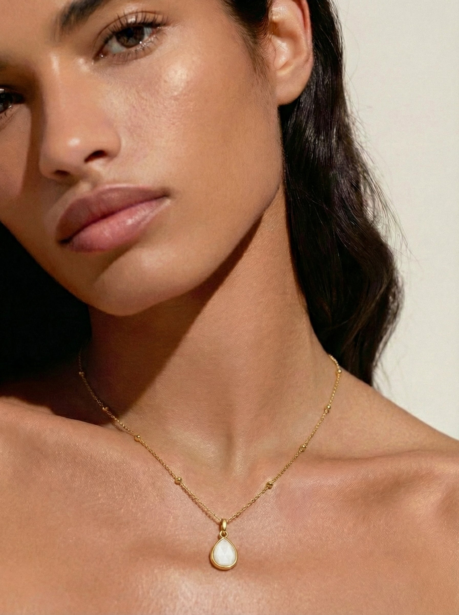 Close-up of a woman wearing a gold necklace with a moonstone pendant against a neutral background