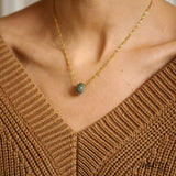 Gold necklace with a green gemstone pendant worn by a person in a brown sweater.