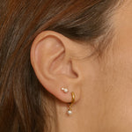 Drop pearl huggies in 18k gold plated silver. The earrings feature a huggie-style design with drop-shaped pearls. The pearls are lustrous and elegantly suspended from the gold plated silver hoops. The hoops have a sleek and polished finish. These earrings are versatile and can be worn for both casual and formal occasions