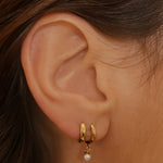 Drop pearl huggies in 18k gold plated silver. The earrings feature a huggie-style design with drop-shaped pearls. The pearls are lustrous and elegantly suspended from the gold plated silver hoops. The hoops have a sleek and polished finish. These earrings are versatile and can be worn for both casual and formal occasions