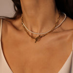 Waterproof 18k gold plated toggle choker.The set includes a sleek and minimalistic 18k gold plated toggle choker with a decorative gold ring and a bar that fits through it to secure the necklace. The choker is layered with a beaded pearl necklace, featuring lustrous white pearls strung on a delicate gold chain. The two necklaces complement each other perfectly, adding a touch of elegance and sophistication to the model's outfit