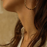 a pair of 18k gold vermeil hoop earrings, featuring a twisted design. The hoops are large in size, yet lightweight, making them comfortable to wear. The gold has a polished finish, reflecting light and enhancing their shine. These striking earrings add a bold and elegant touch to any outfit.