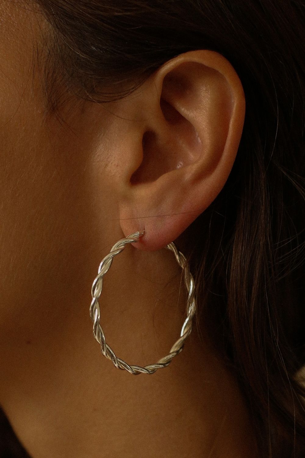 a pair of silver hoop earrings, featuring a twisted design. The hoops are large in size, yet lightweight, making them comfortable to wear. The silver has a polished finish, reflecting light and enhancing their shine. These striking earrings add a bold and elegant touch to any outfit.