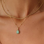 Gold necklace with a green teardrop pendant on a person's neck