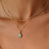Gold necklace with a green teardrop pendant on a person's neck