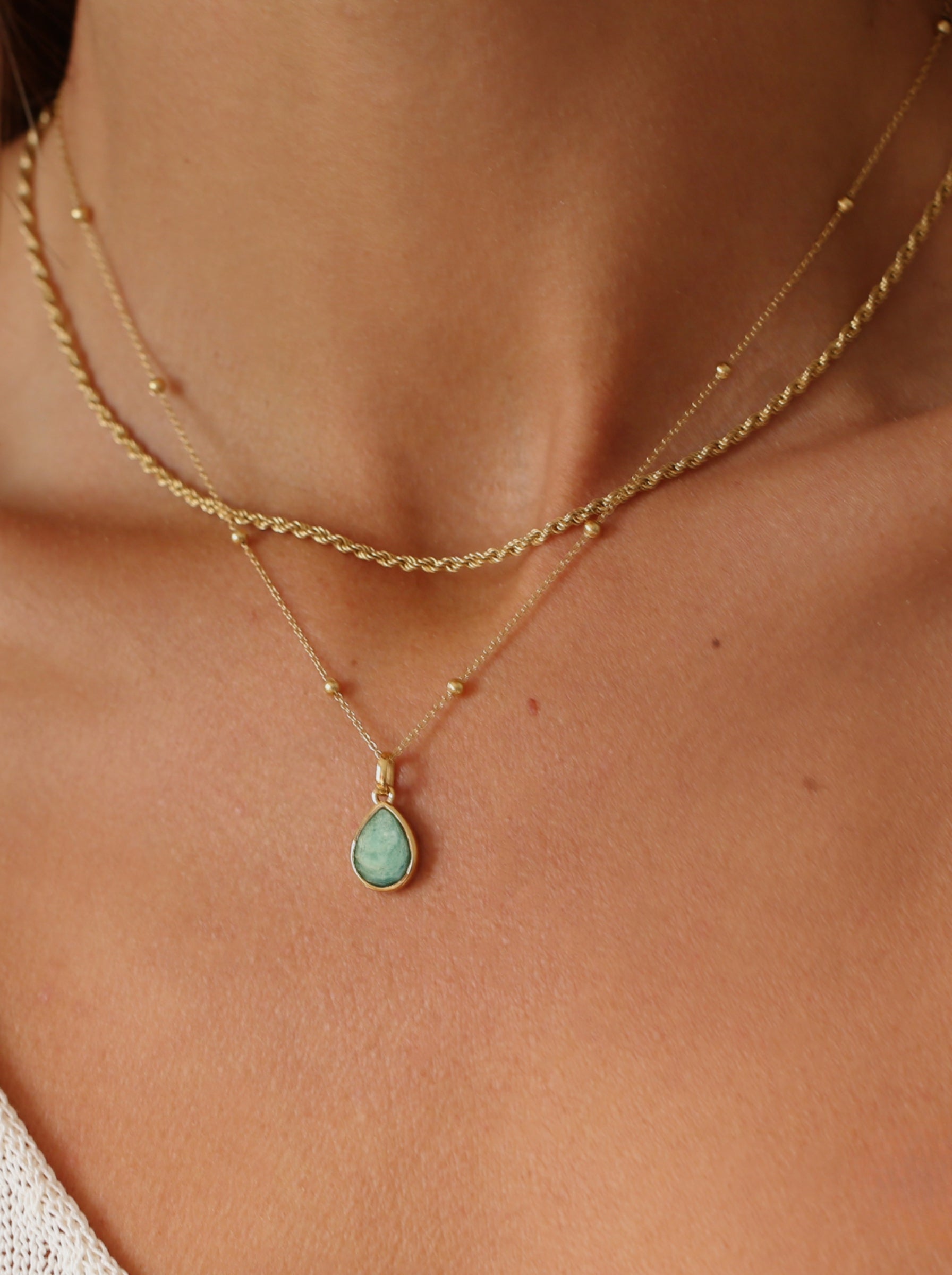 Gold necklace with a green teardrop pendant on a person's neck