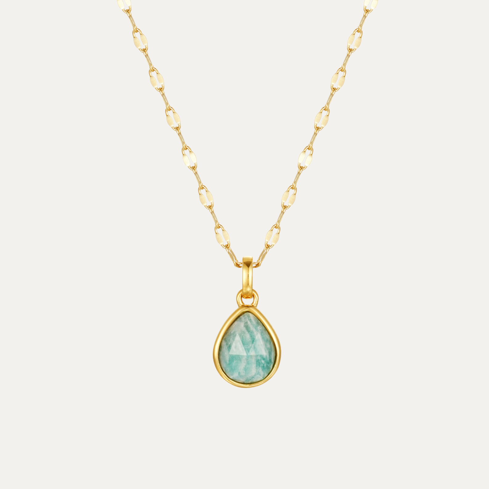 Gold necklace with a teardrop-shaped green gemstone pendant on a white background