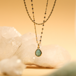 Gold necklace with a green teardrop pendant on a soft yellow background