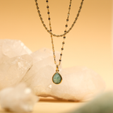 Gold necklace with a green teardrop pendant on a soft yellow background