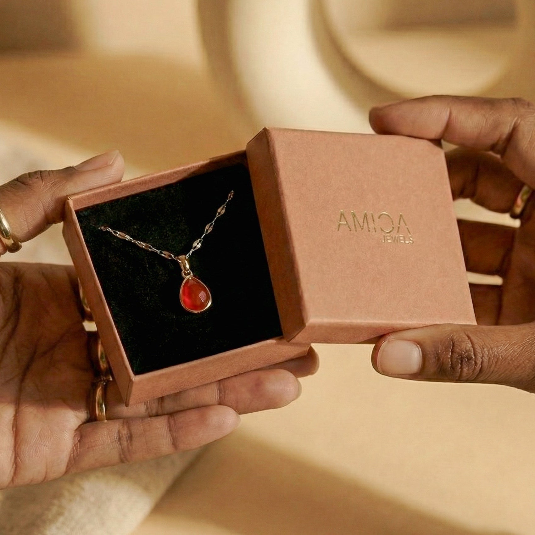 Necklace with a red pendant in an open jewelry box held by hands.