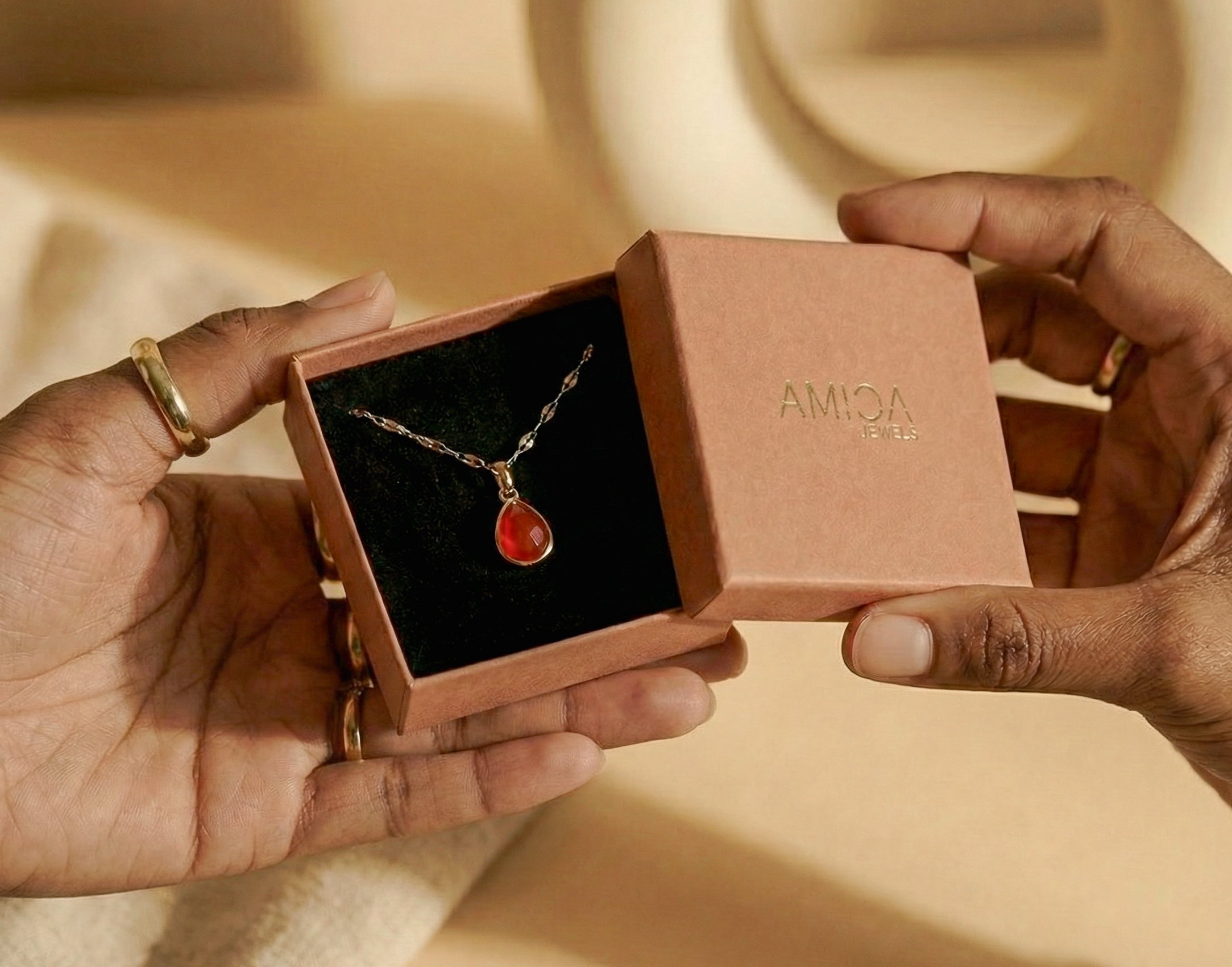 Necklace with a red pendant in an open jewelry box held by hands.