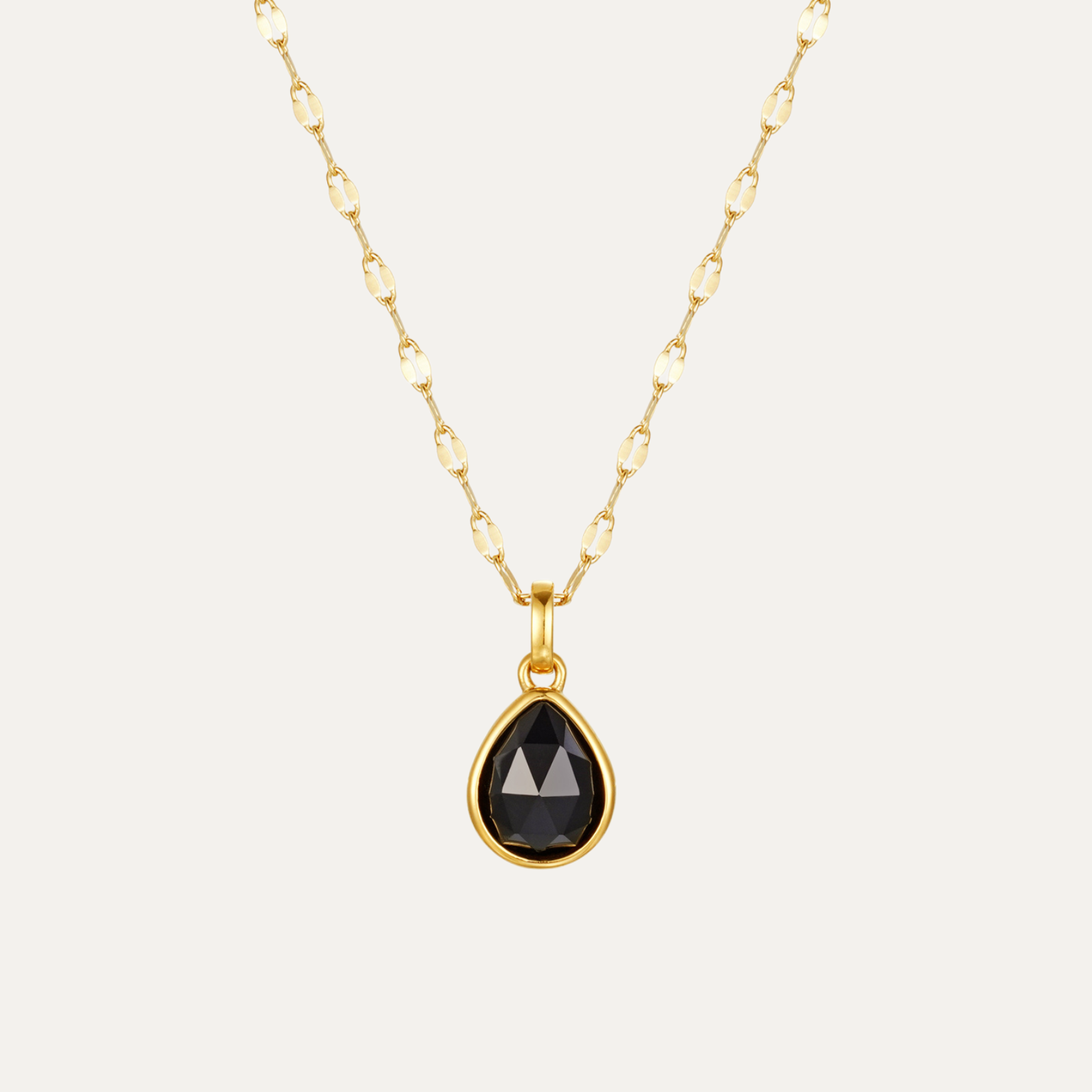 Gold necklace with a black teardrop pendant on a light gray background