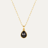 Gold necklace with a black teardrop pendant on a light gray background