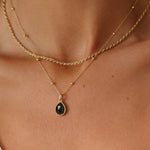 Gold necklace with a black pendant on a person's neck