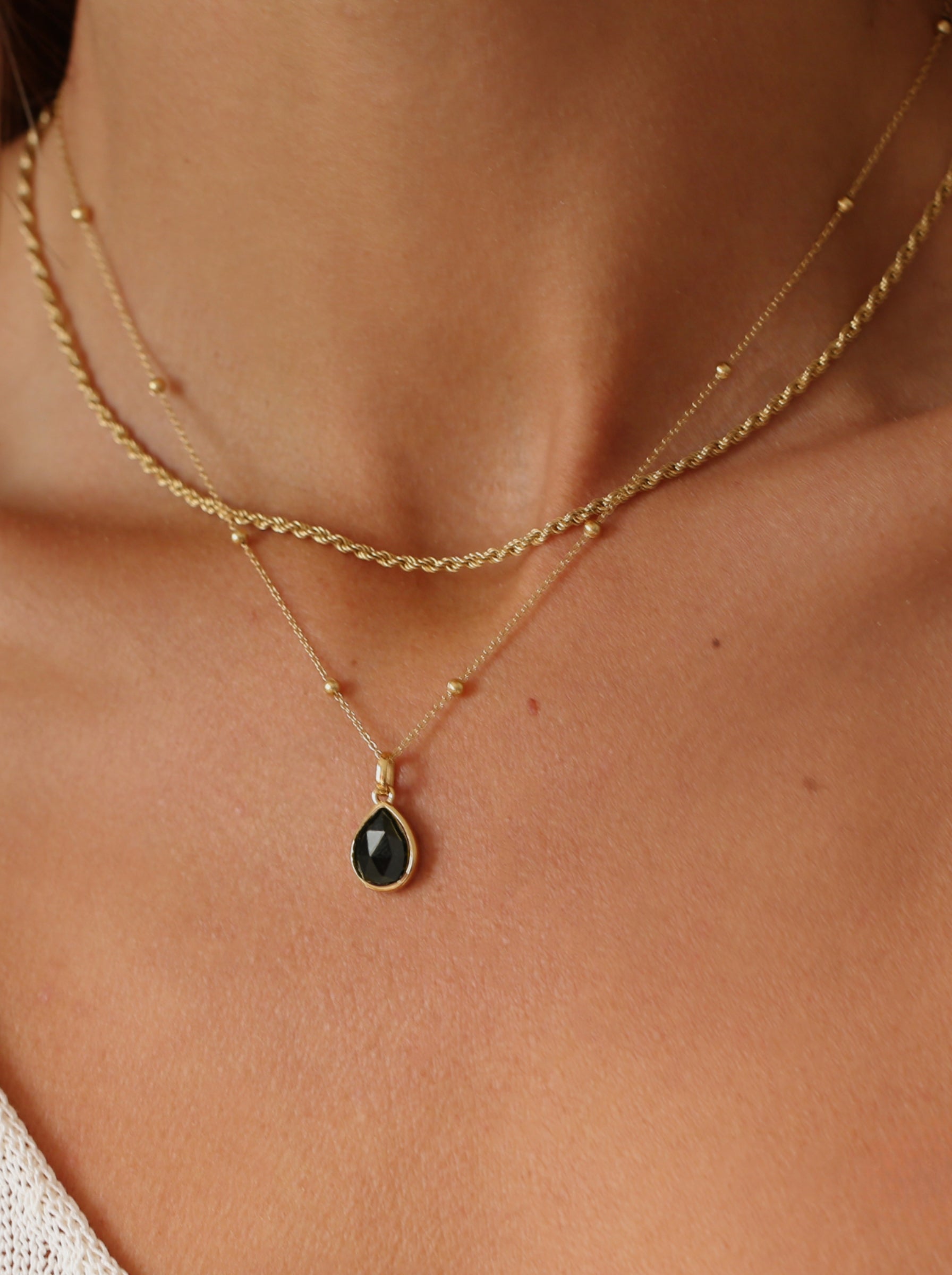 Gold necklace with a black pendant on a person's neck