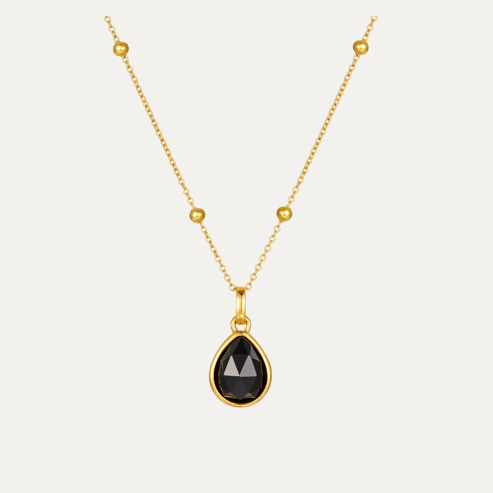 Gold necklace with a black teardrop pendant on a light gray background