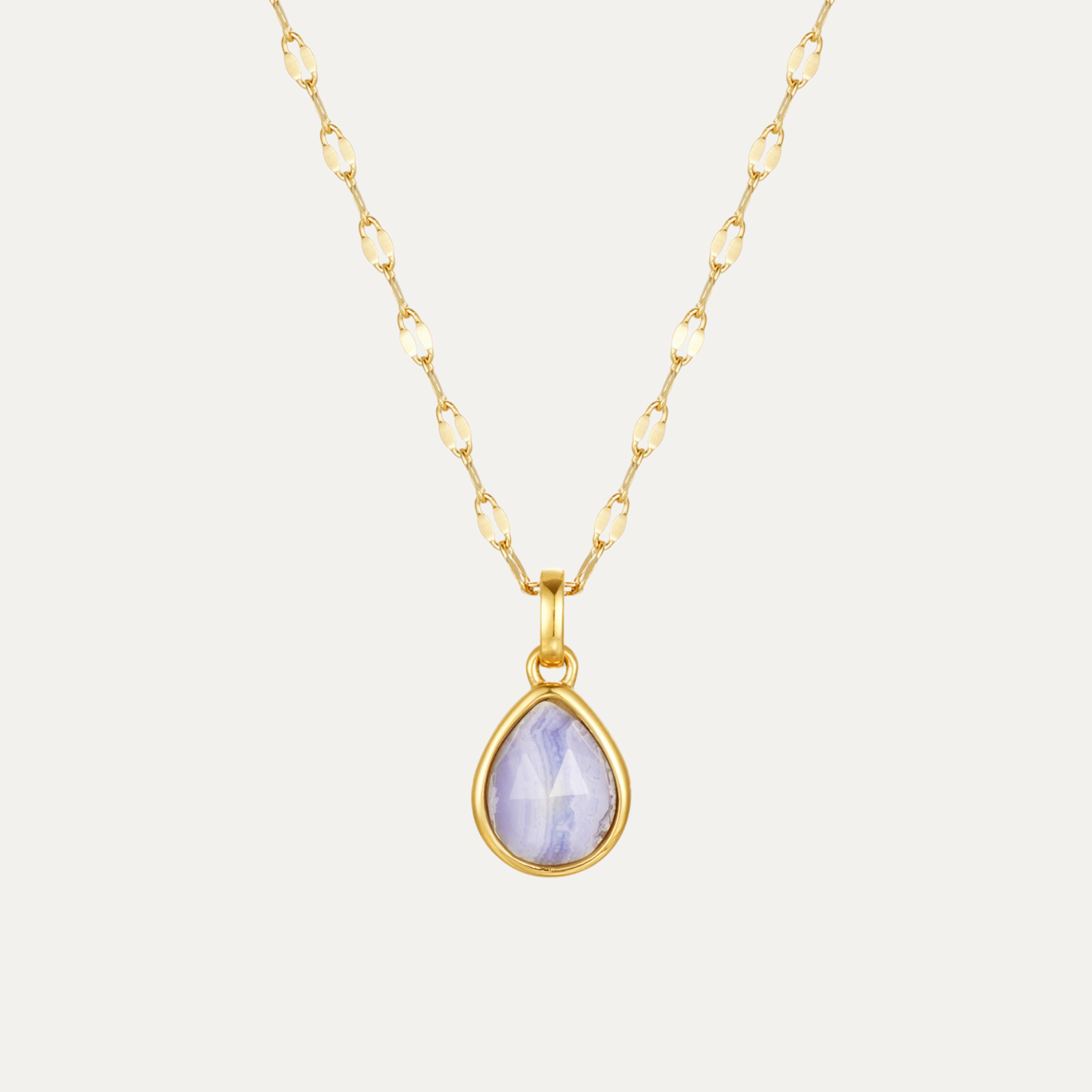 Gold necklace with a teardrop-shaped purple gemstone pendant on a light gray background