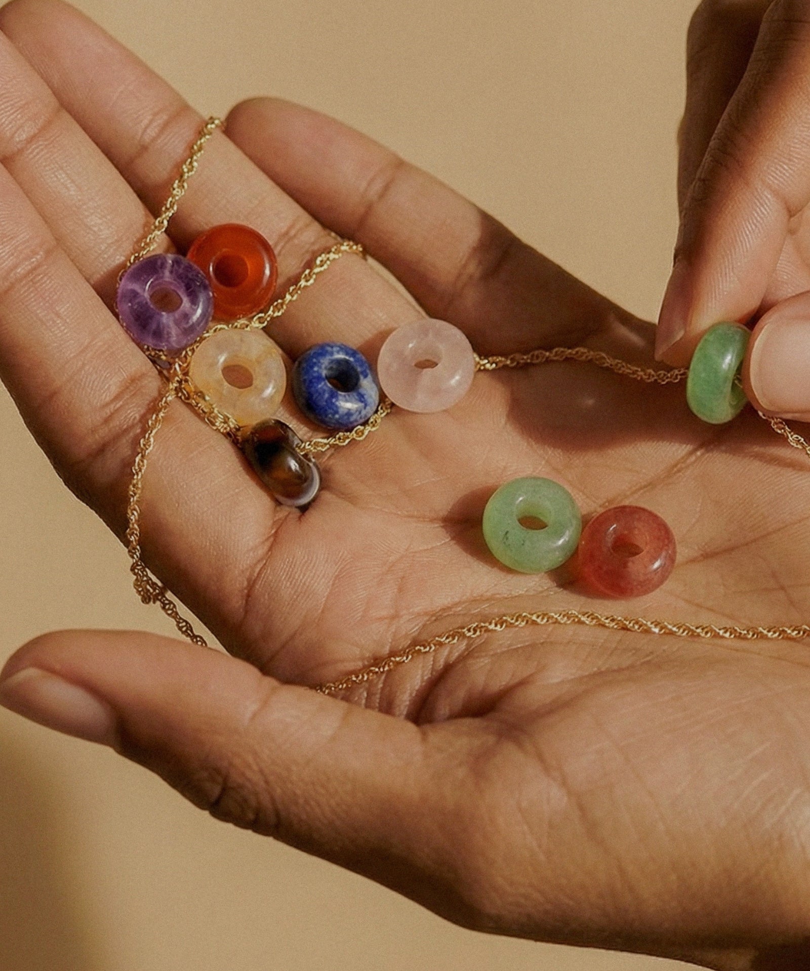 Hands holding a gold chain with multiple colorful donut gemstone charms