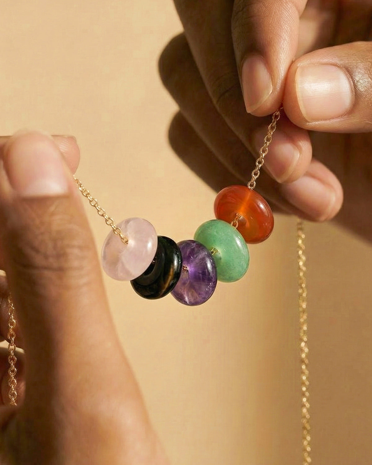 Hands holding a gold chain with five mixed gemstone donut charms