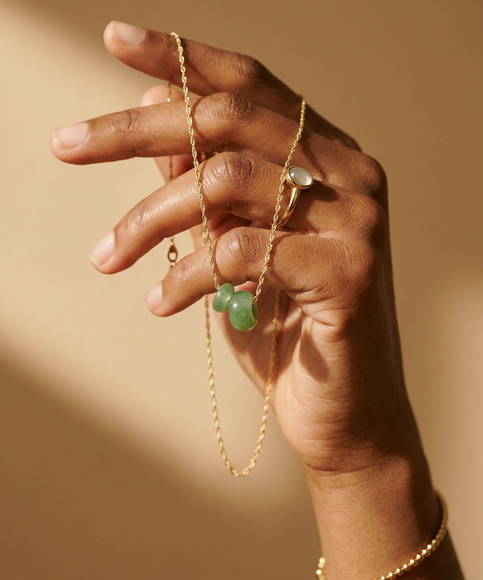 Hand holding a gold chain with Green Aventurine donut charms