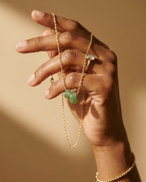 Hand holding a gold chain with Green Aventurine donut charms
