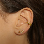 a croissant ear cuff in 18k gold plated silver. The ear cuff features a unique croissant-shaped design that wraps around the earlobe. It is made of high-quality gold plated silver with a polished finish, giving it a luxurious and elegant look. The cuff is designed to be worn without the need for a piercing, making it a trendy and versatile accessory.