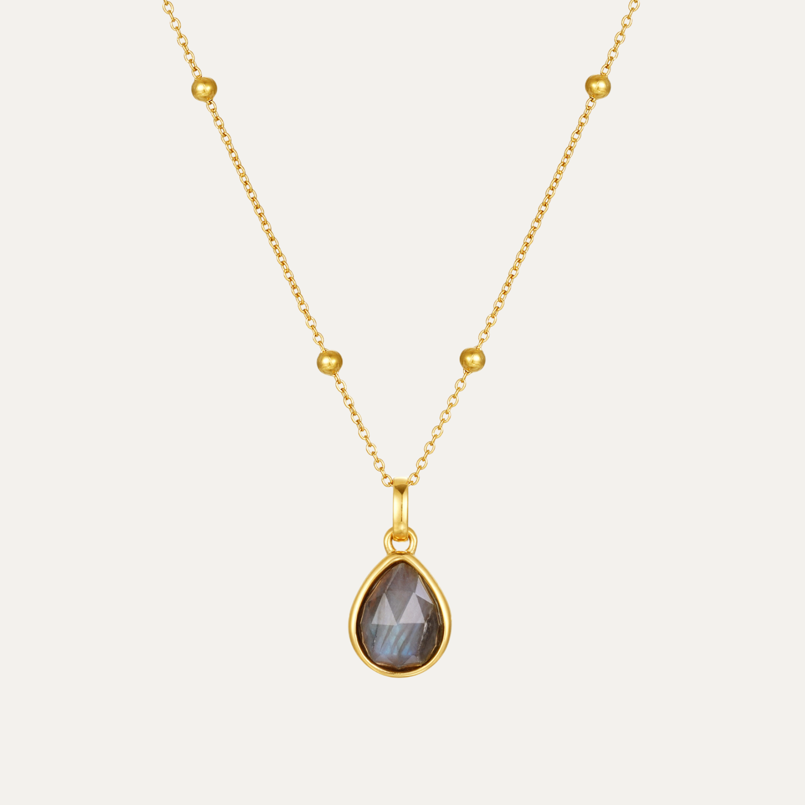Gold necklace with a teardrop-shaped pendant on a light gray background