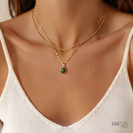 Close-up of a woman wearing a gold necklace with a green pendant, branded 'AMICA'.