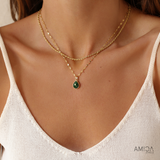 Close-up of a woman wearing a gold necklace with a green pendant, branded 'AMICA'.