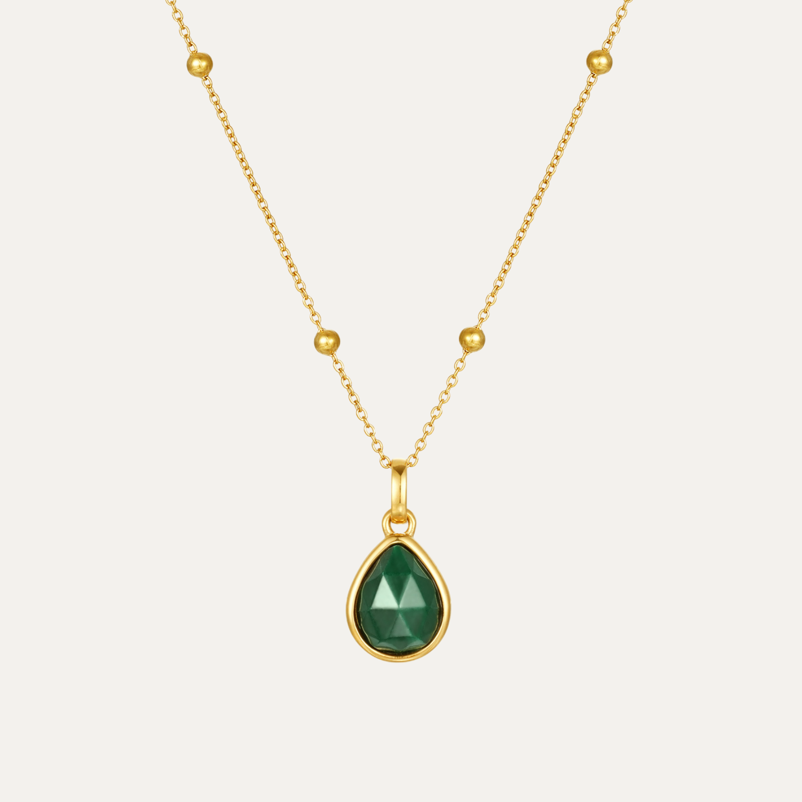 Gold necklace with a green teardrop pendant on a light gray background