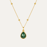 Gold necklace with a green teardrop pendant on a light gray background