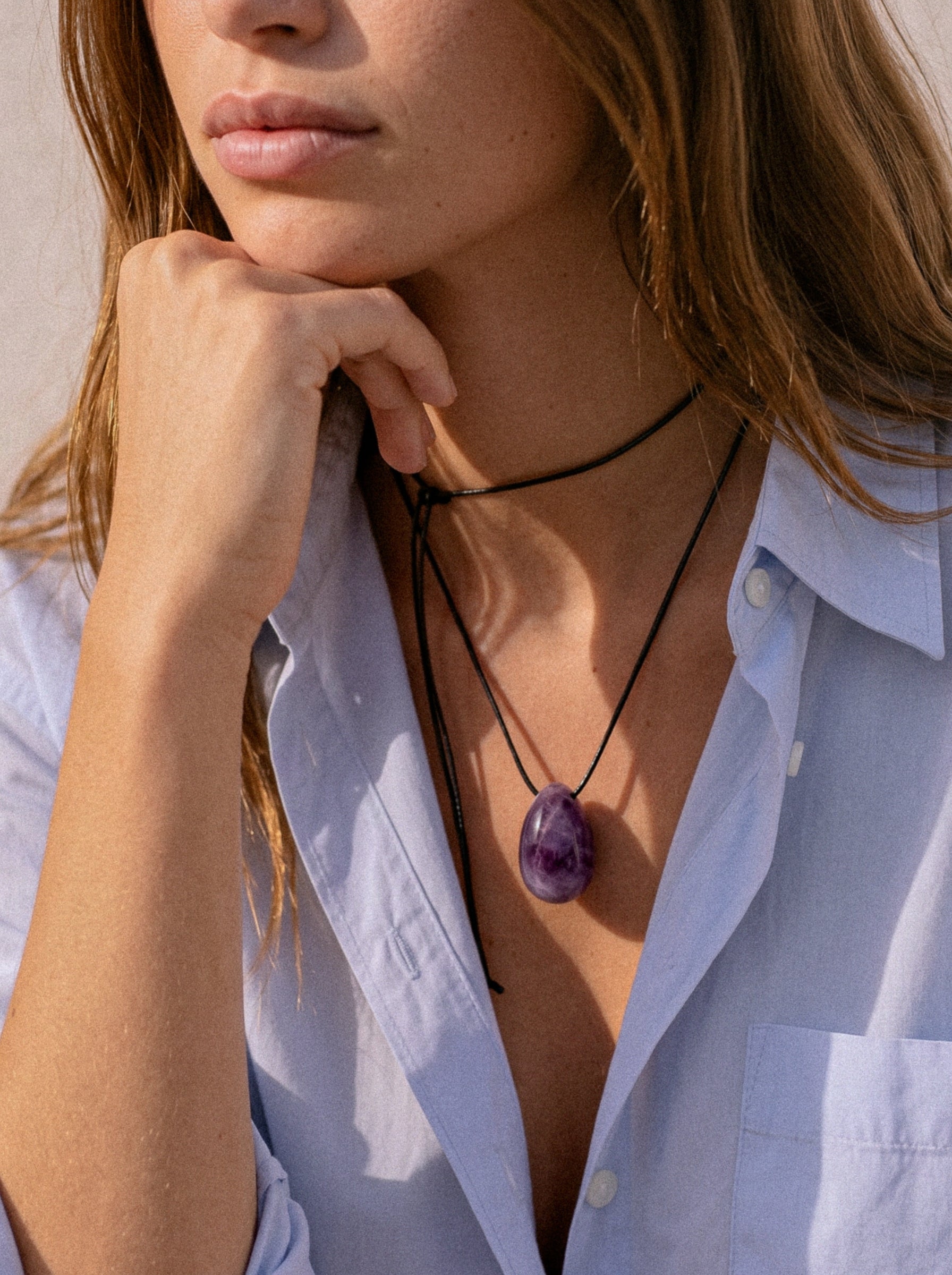 Close-up of model wearing an Amethyst pendant with hand at chin