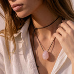 Rose Quartz pendant and black silk cord draped across a hand