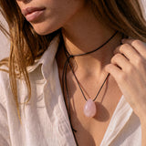 Rose Quartz pendant and black silk cord draped across a hand