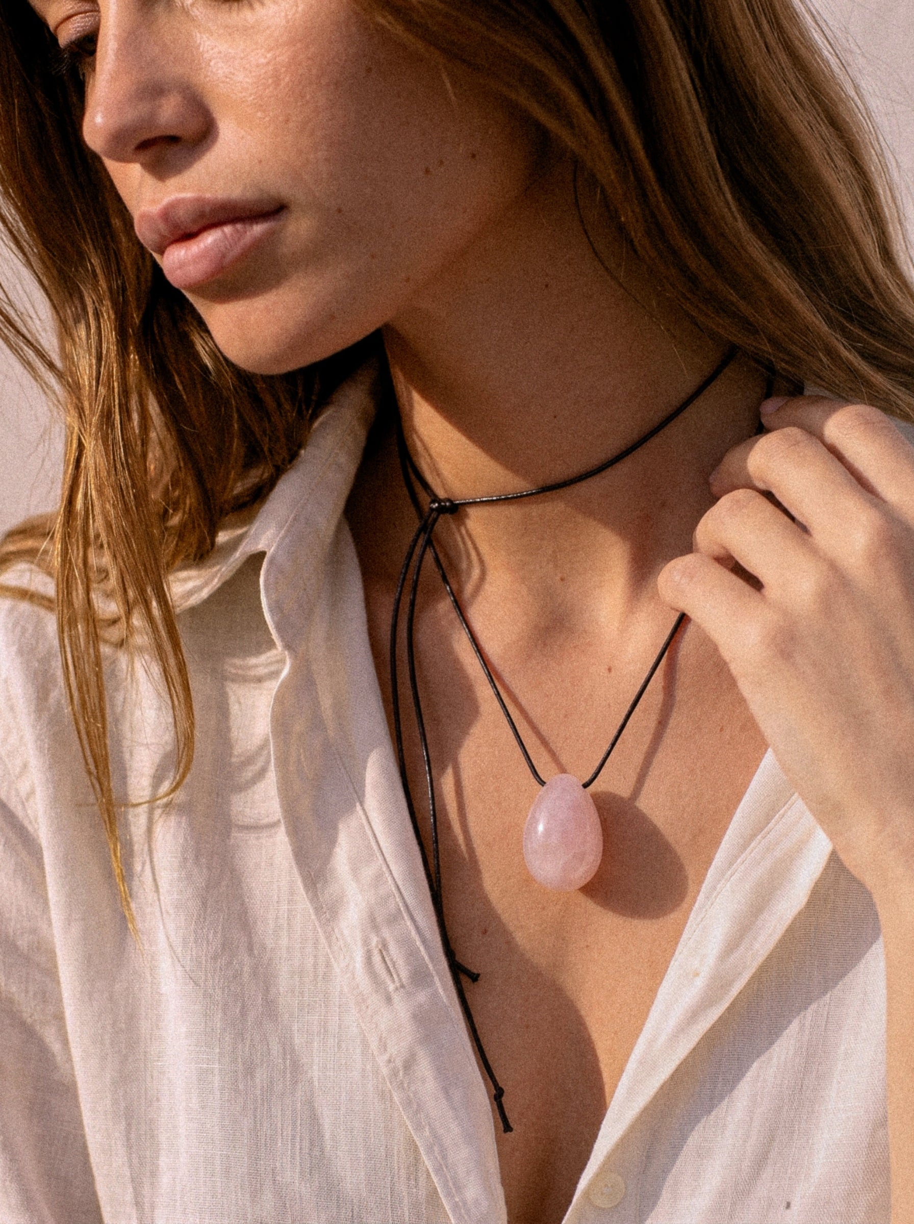 Rose Quartz pendant and black silk cord draped across a hand