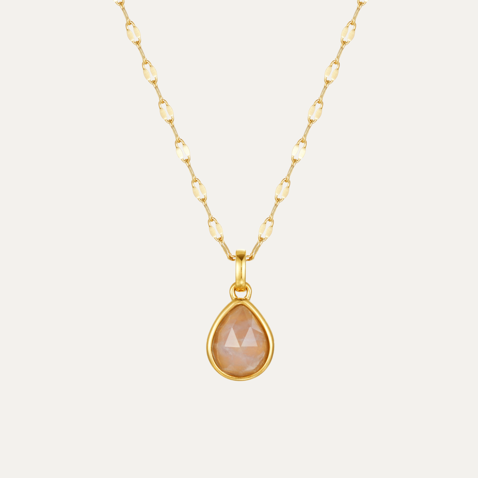 Gold necklace with a rose quartz teardrop-shaped pendant on a light gray background