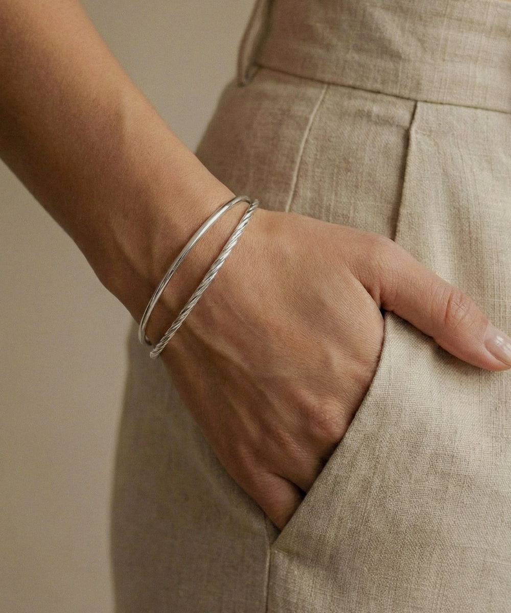 Close-up of a hand wearing two silver bracelets on a neutral background