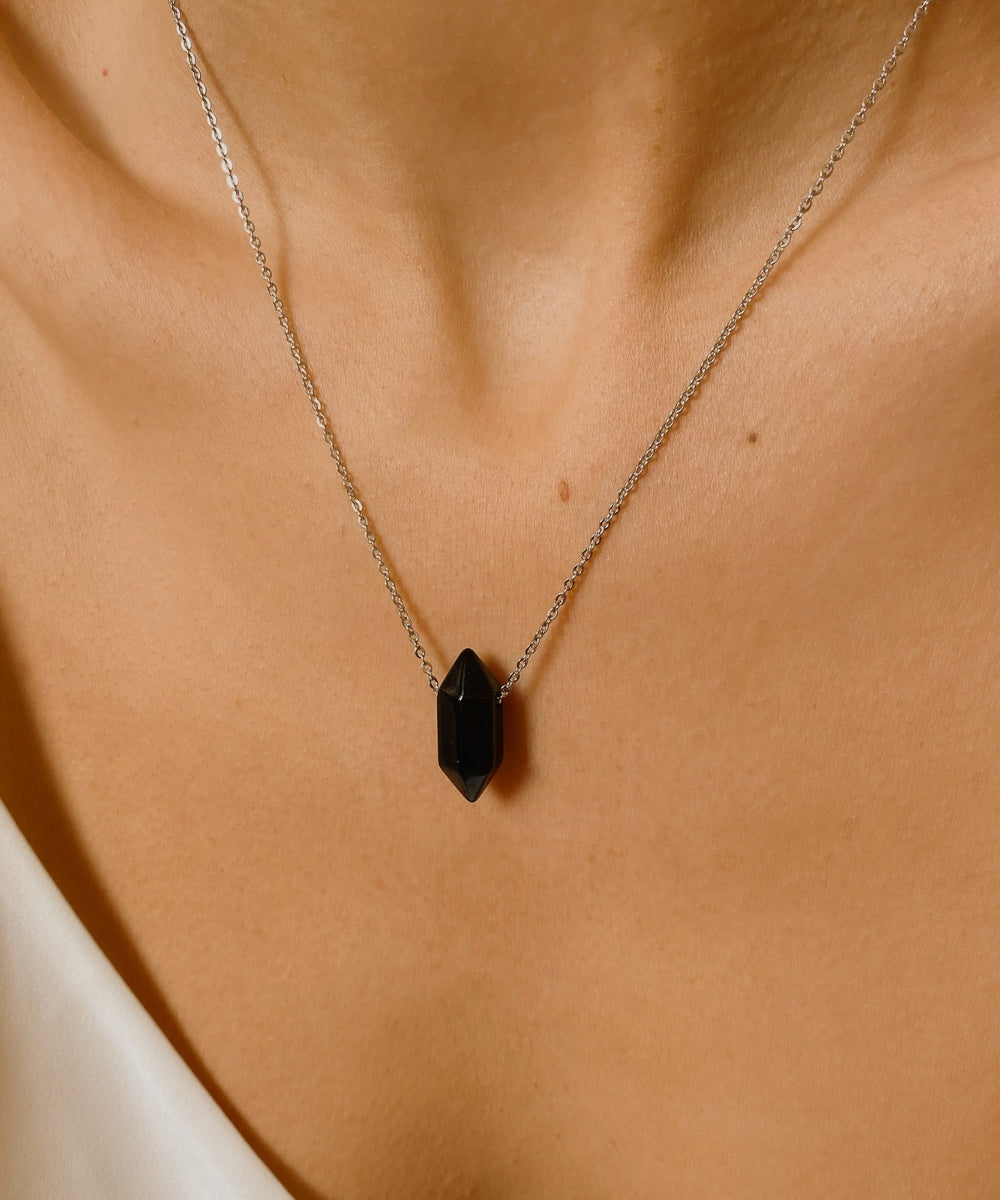 Black obsidian crystal necklace. The necklace features a pointed black obsidian crystal pendant attached to a gold chain, creating a stunning and eye-catching piece of jewelry.